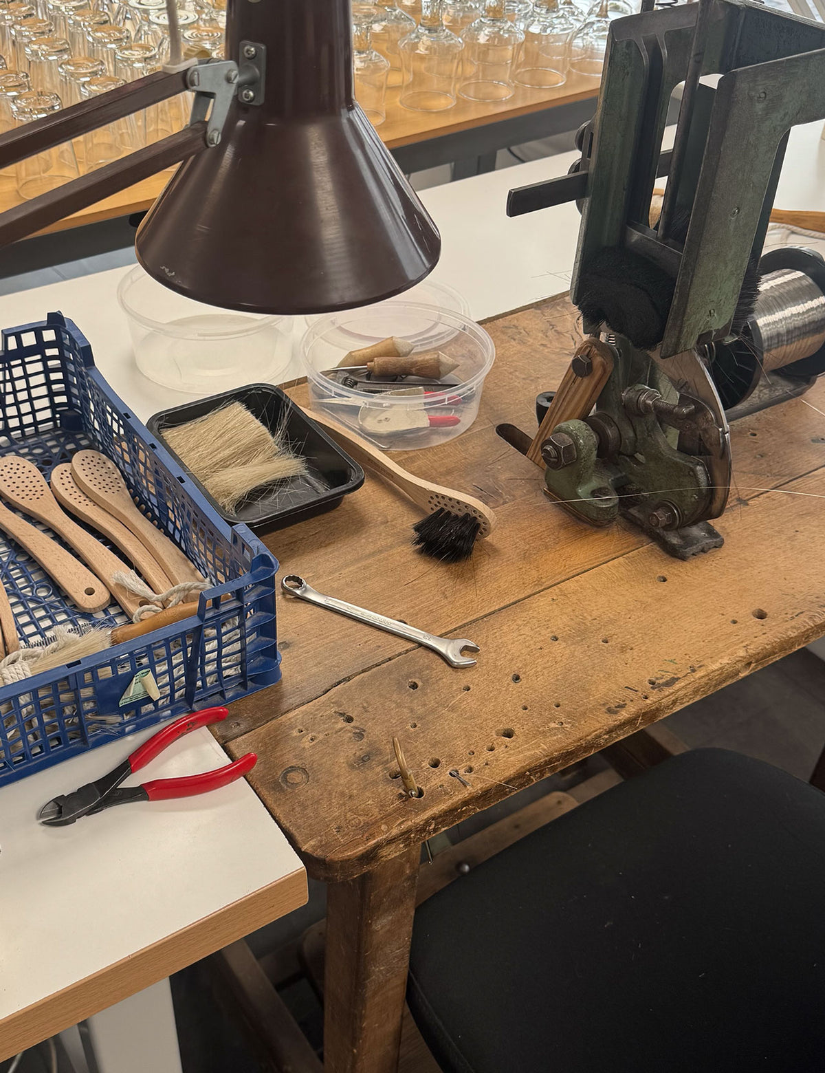 Værkstedsbord med børsteskafter, værktøj og en gammel maskine under arbejdslampen